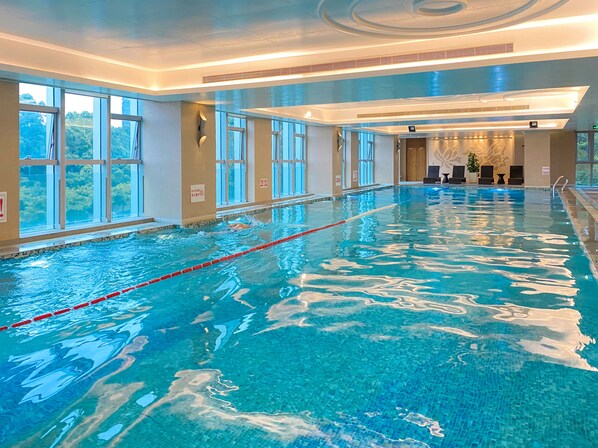 An indoor swimming pool with clear water, multiple lanes, and large windows offering views of the outdoors.