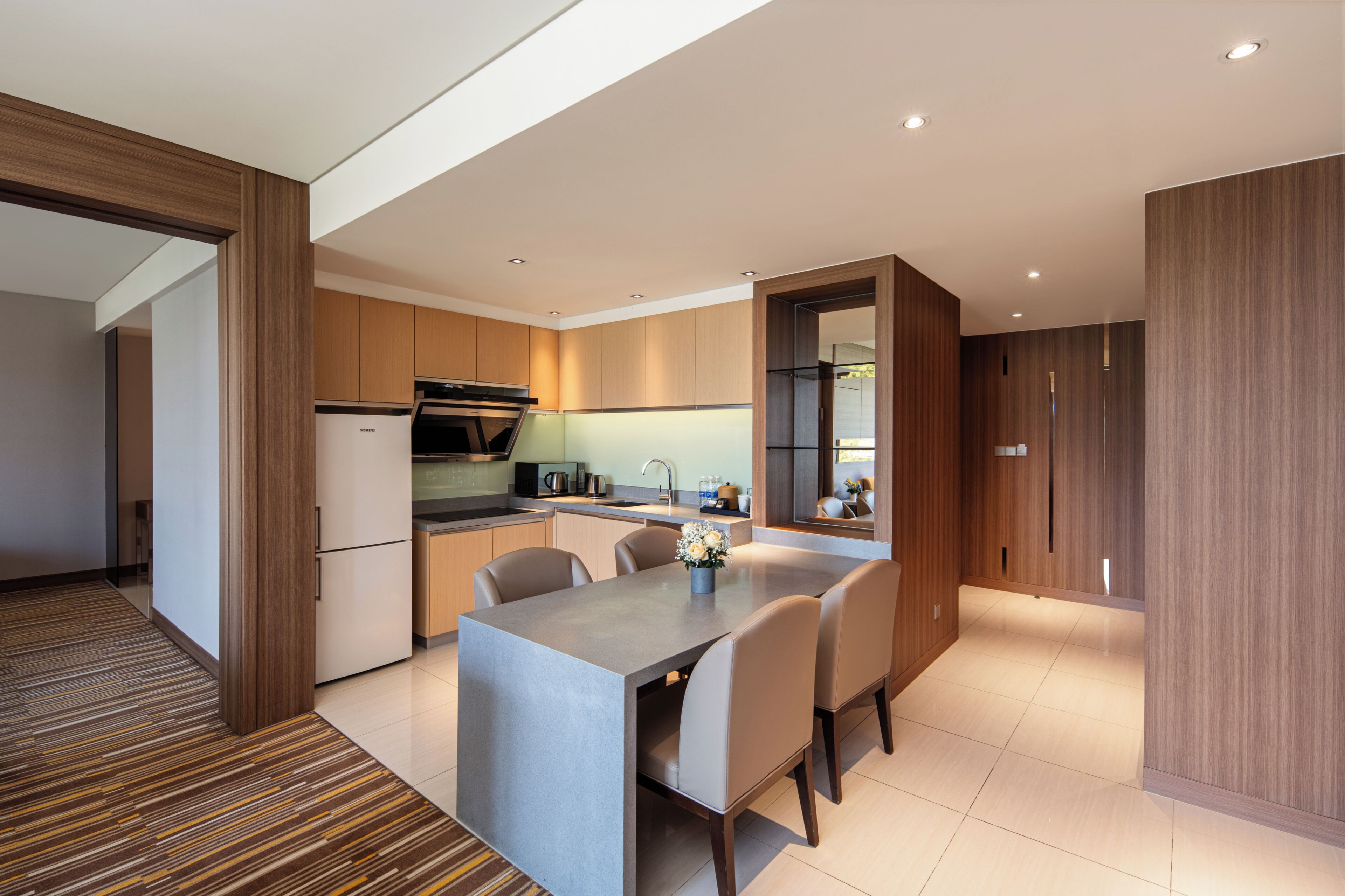 A modern kitchen with a built-in oven, a dining area with a table and chairs, and wooden cabinetry.