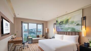 A hotel room with a large bed, a desk with a chair, a TV, and a painting on the wall.