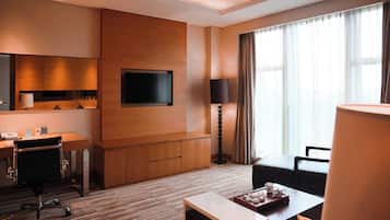 Habitación de hotel con escritorio de madera, televisor de pantalla plana montado en la pared, lámpara y zona de estar con mesa y sillas.