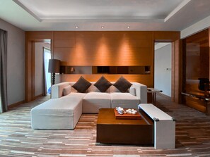 A modern hotel room with a sectional sofa, a coffee table, and a large mirror.