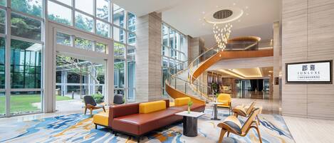 A spacious lobby with a modern staircase, comfortable seating, and large windows offering views of the outdoors.