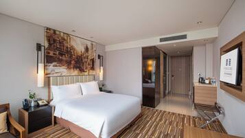 Quarto de hotel com cama grande, mesas de cabeceira, TV fixada na parede e um quadro.