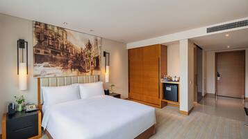 Habitación de hotel con una cama grande, mesitas de noche, televisor montado en la pared, armario y una kitchenette pequeña.