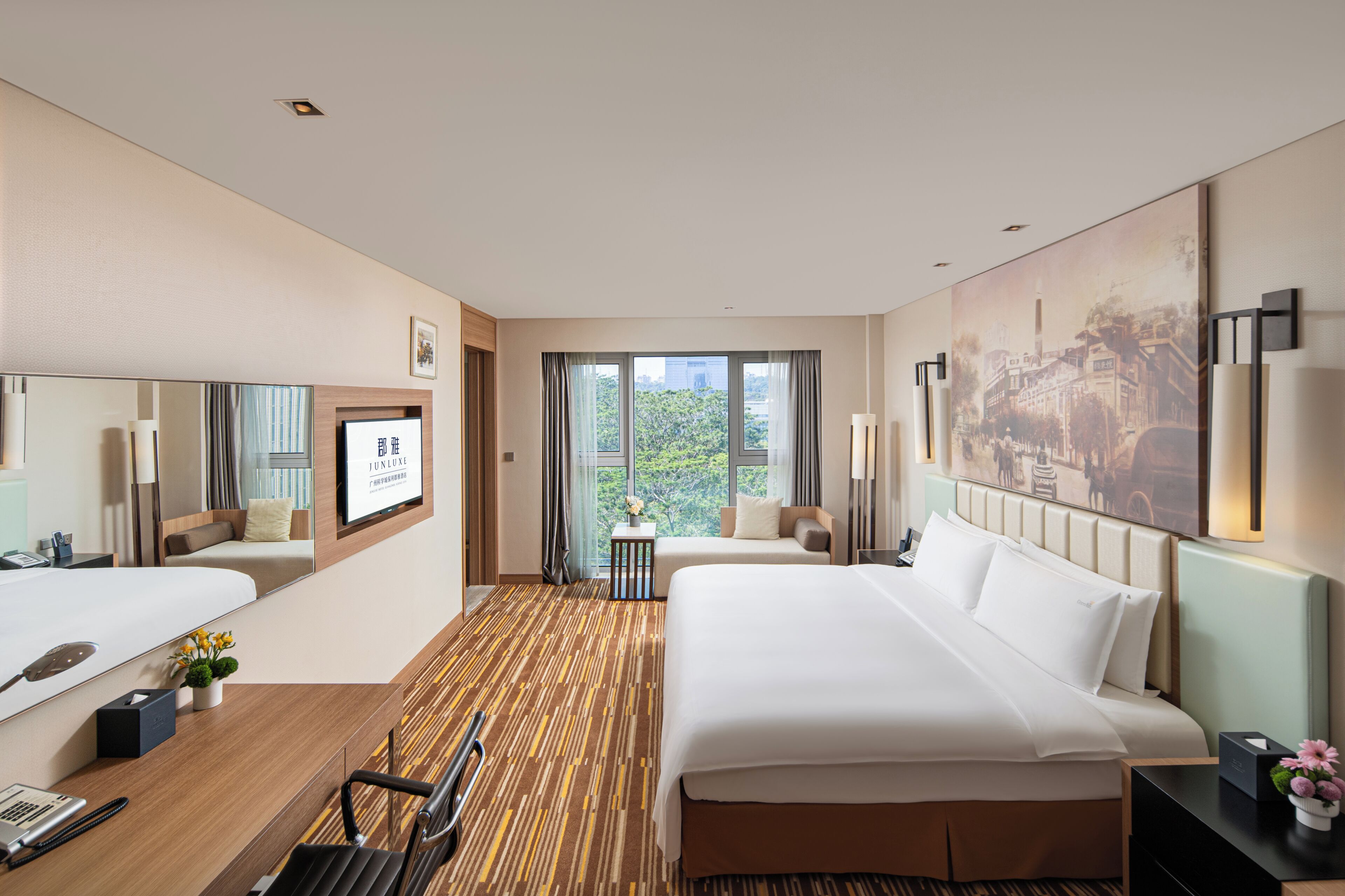 A hotel room with two beds, a desk, a chair, a window with a view, and a painting on the wall.