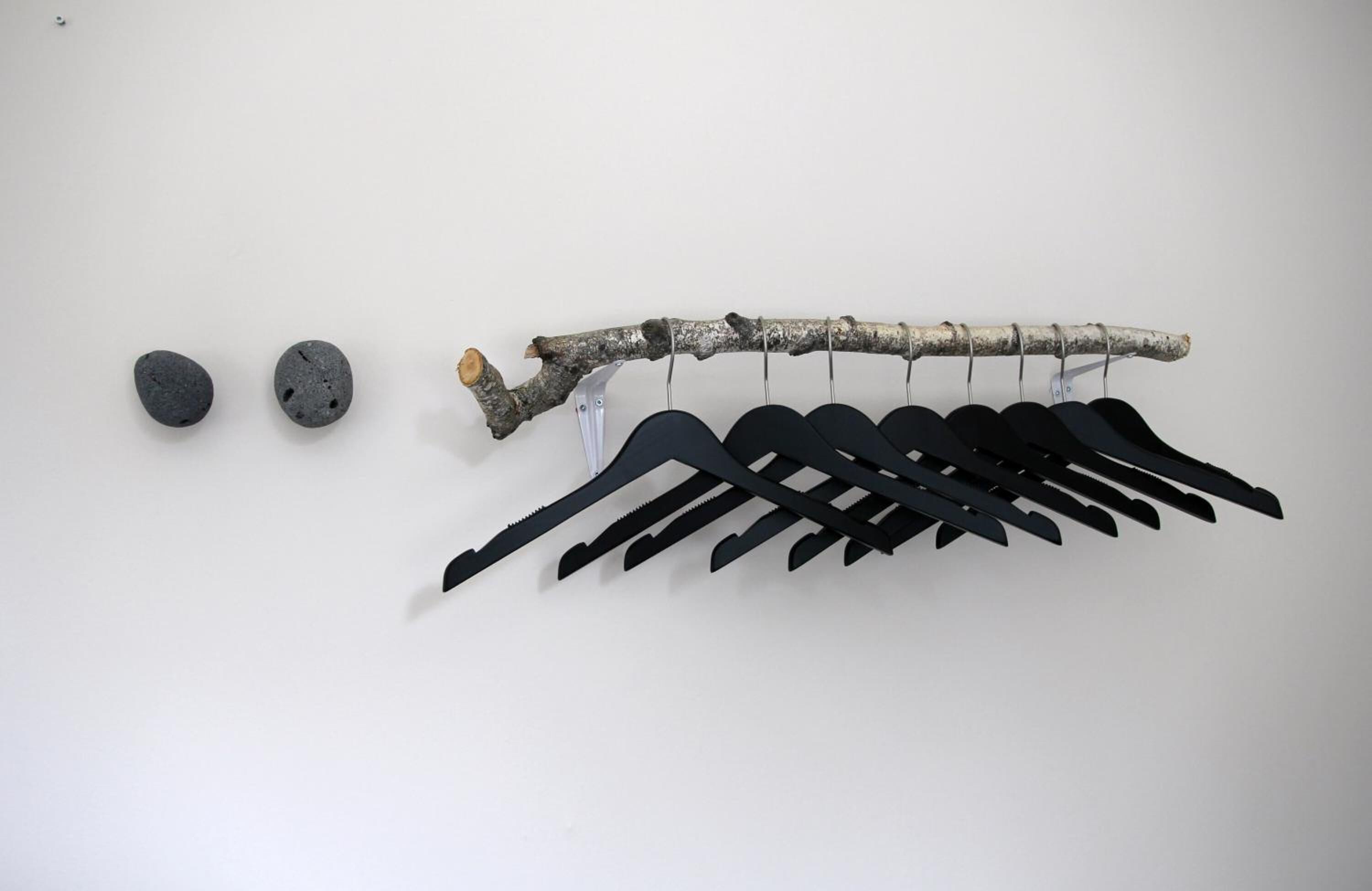 A branch with black hangers and two gray stones on a white background.