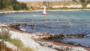 Un muelle se extiende sobre el agua, con un velero y personas a bordo.