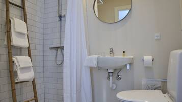 A bathroom with a shower, toilet, sink, and a ladder with towels.