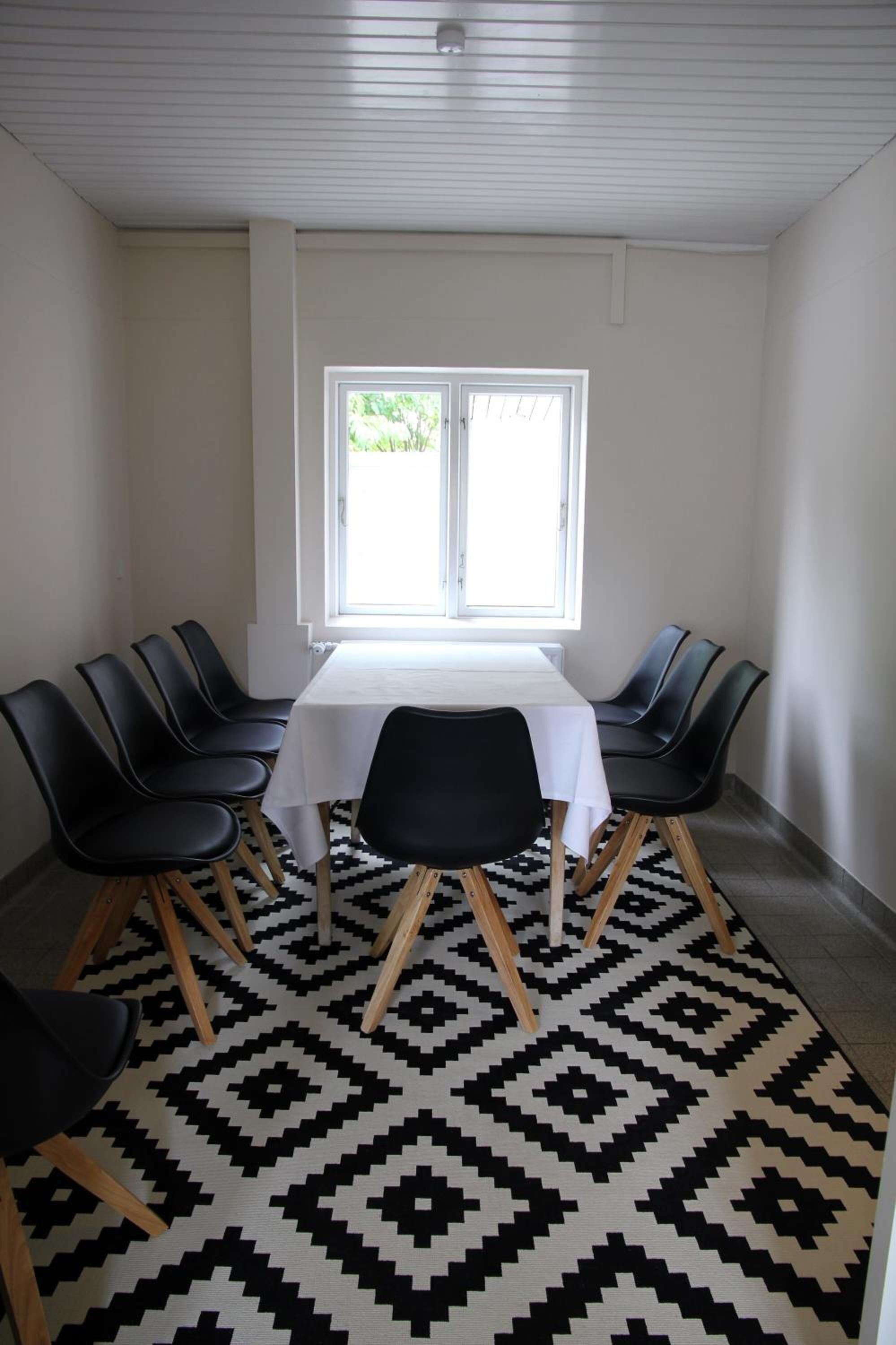 A dining area with a table and chairs, a window, and a patterned rug.