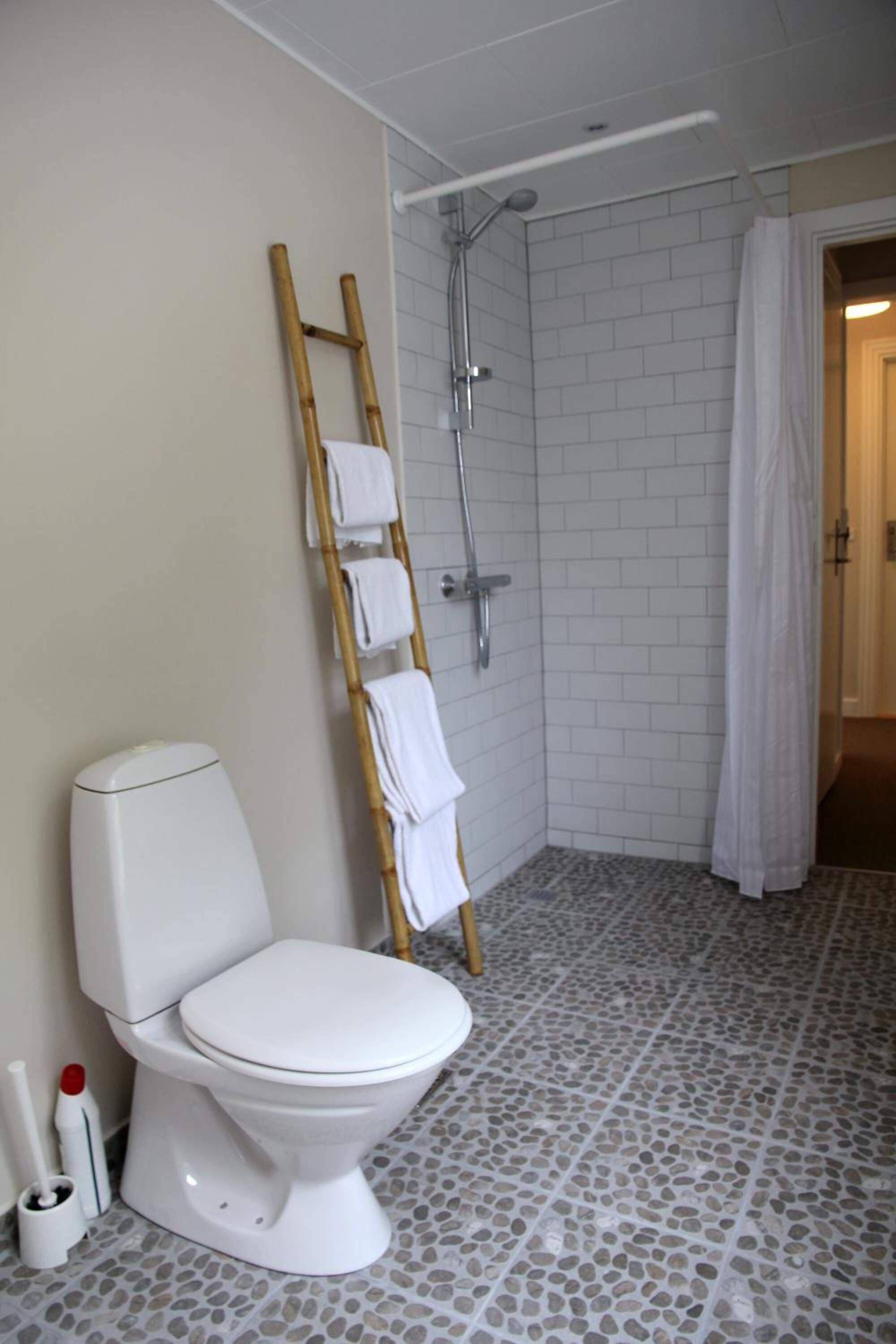 Un baño con inodoro, ducha y escalera de bambú, además de suelo de baldosas.