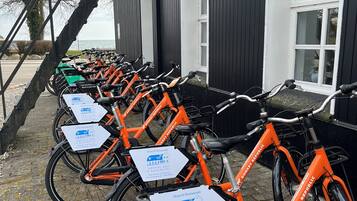 A row of orange bicycles parked outside a building with signs indicating a hotel and restaurant.