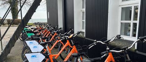 A row of orange bicycles parked outside a building with signs indicating a hotel and restaurant.