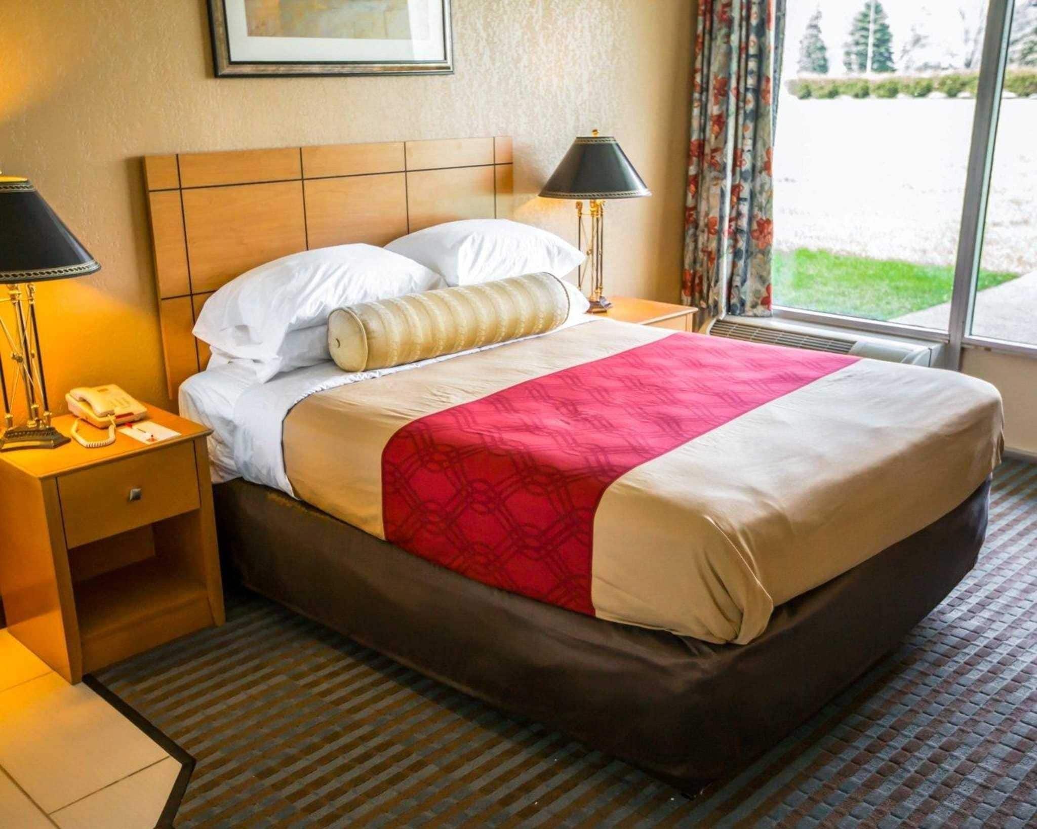 Una camera d'albergo con un letto, comodini, una lampada e una finestra con tende.