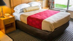 A hotel room with a bed, bedside tables, a lamp, and a window with curtains. - Econo Lodge Shorewood (Joliet)