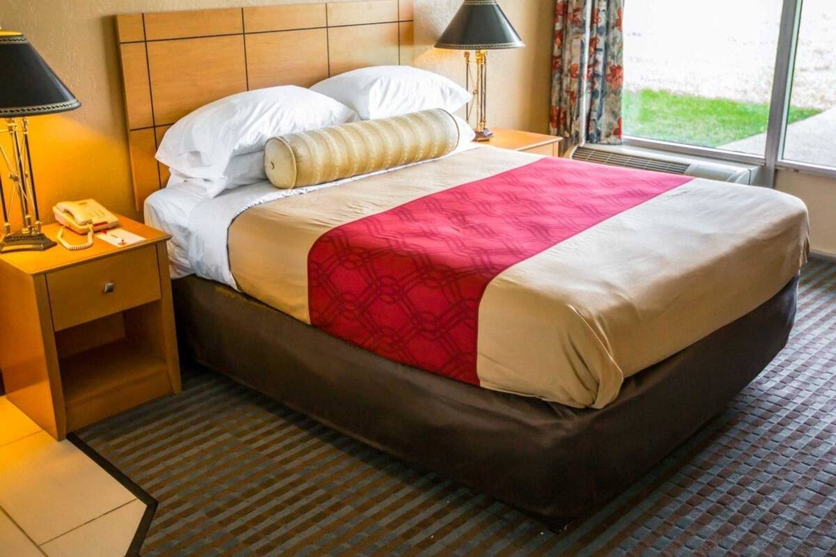 Una habitación de hotel con cama, mesitas de noche, lámpara y ventana con cortinas.