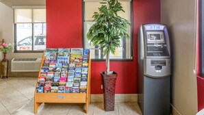 A travel information stand with brochures, a potted plant, and an ATM machine in a room with red walls. - Econo Lodge Shorewood (Joliet)