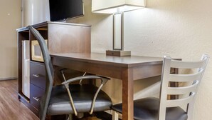 A hotel room with a wooden desk, a black chair, a white chair, a television, and a lamp. - Econo Lodge Shorewood (Joliet)