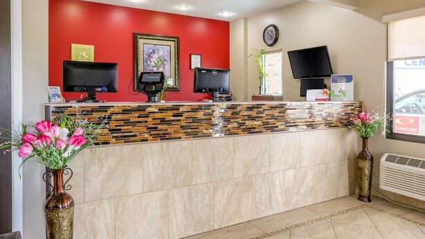 A reception desk with two monitors, a clock, and a window with a view of a car. - Econo Lodge Shorewood (Joliet)