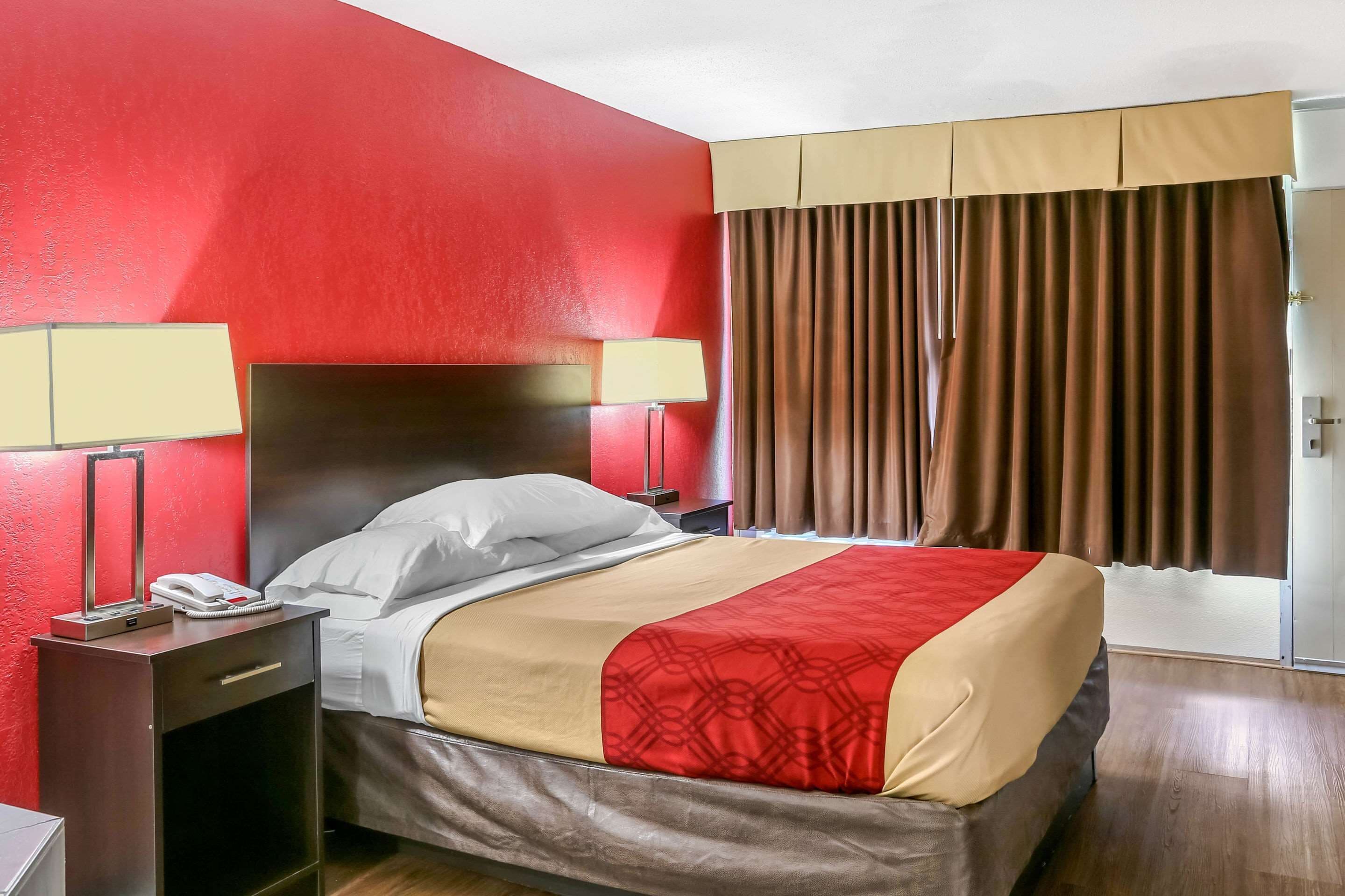 Habitació d'hotel amb un llit, dues taules de nit amb làmpades, un telèfon i una finestra amb cortines.