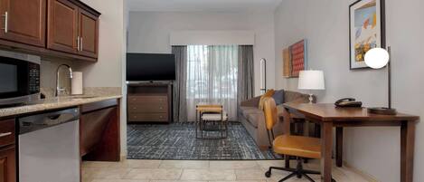A compact hotel room with a kitchenette, a dining area, and a seating space.