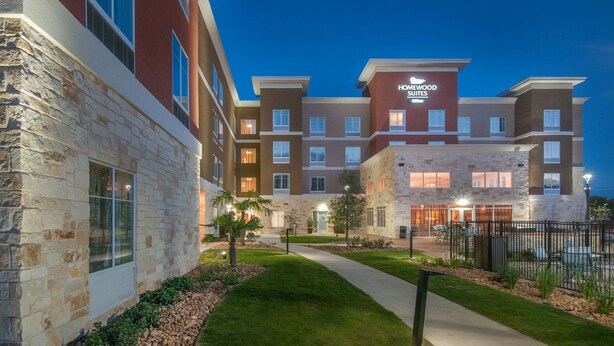 A multi-story hotel with a stone facade, a central courtyard, and a sign reading "Homewood Suites".