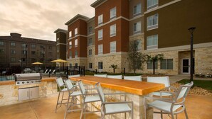 An outdoor bar area with a stone countertop, bar stools, and a grill.