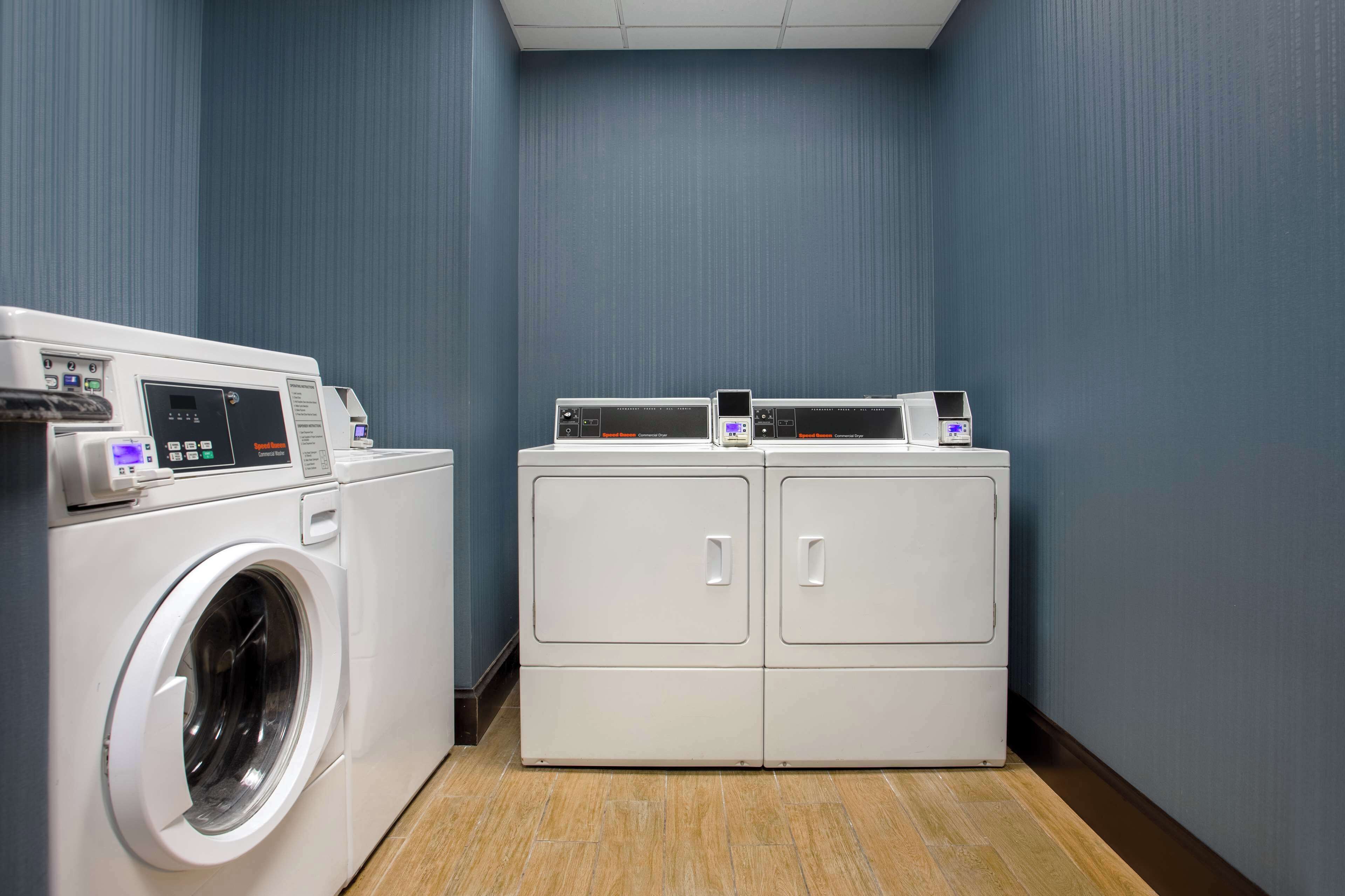 A laundry room with a front-loading washer and two stacked dryers.
