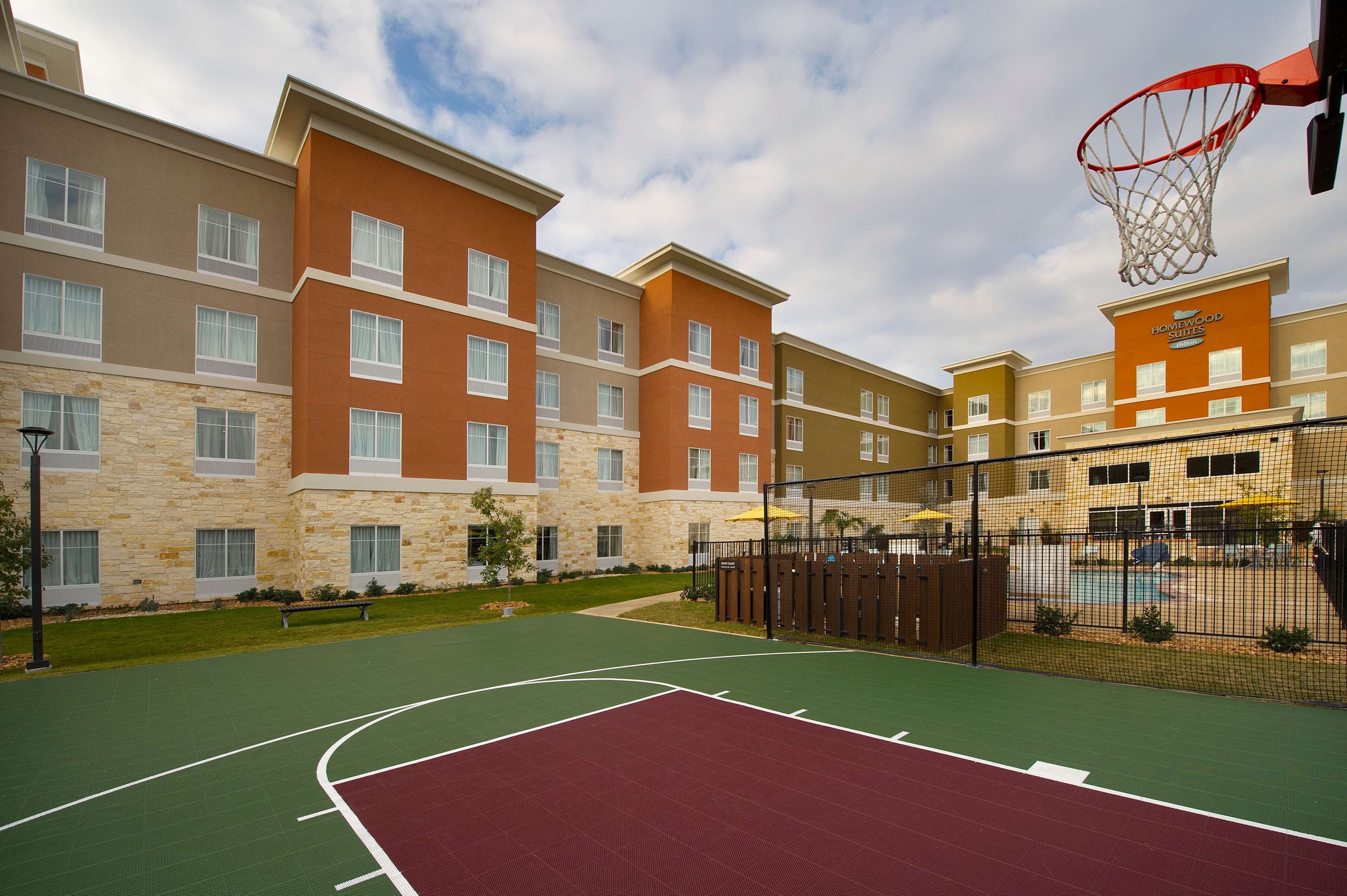 Una cancha de baloncesto junto a un hotel de varios pisos con fachada de piedra y un área de piscina.