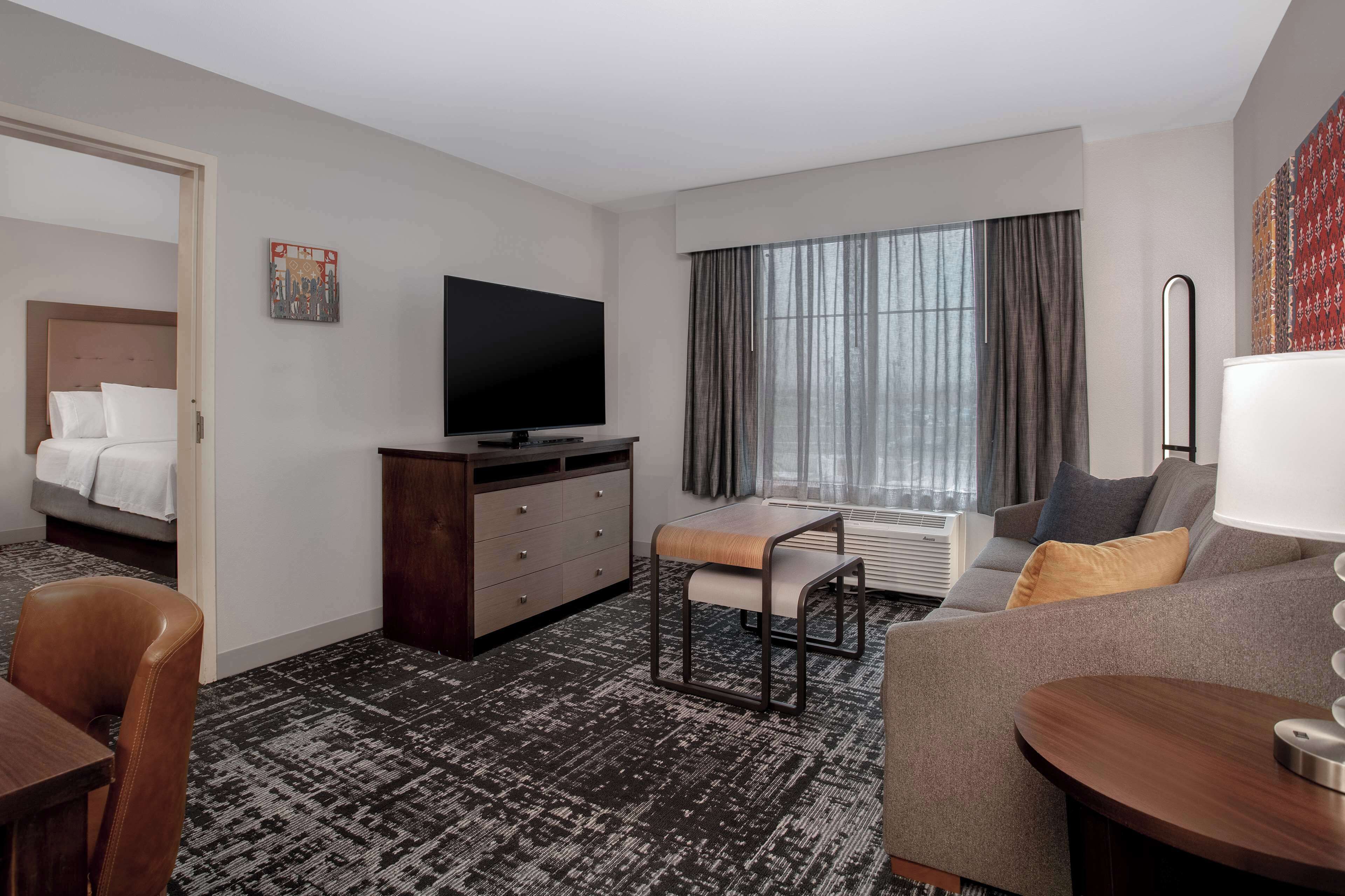 Habitación de hotel con cama, televisión, sofá, una mesita y ventana con cortinas.