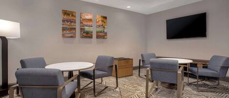 A hotel room with a round table, four chairs, a flat-screen TV, and three paintings on the wall.