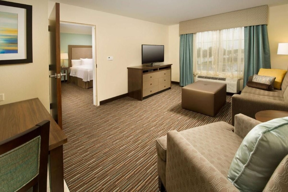 A hotel room with a bed, a TV, a sofa, a desk, and a window with curtains.