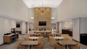 A spacious hotel lobby with a central seating area, a flat-screen TV mounted on a stone wall, and a modern chandelier.