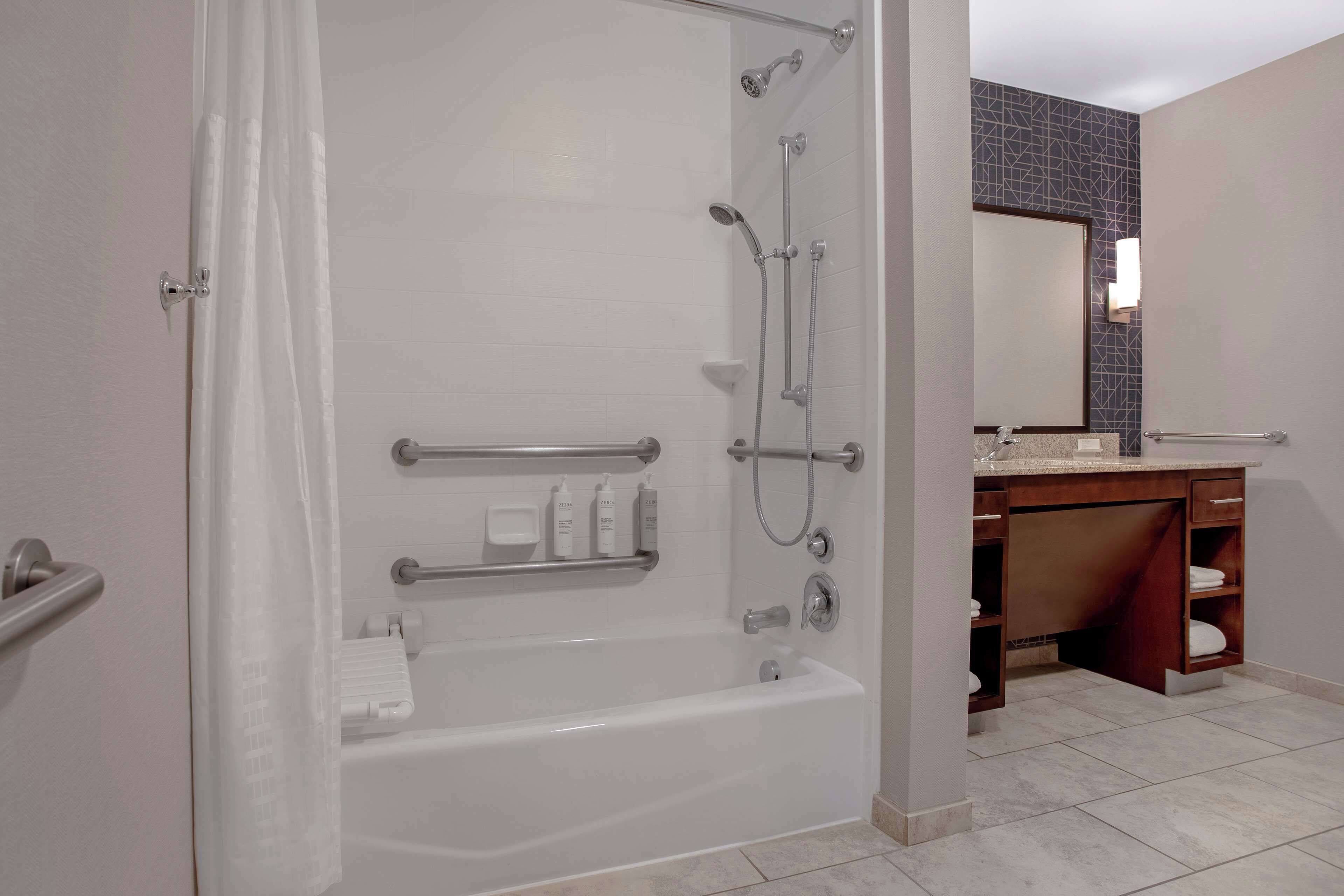 Un baño moderno con cabina de ducha, barras de apoyo, bañera y tocador con espejo.