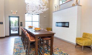 Un espace repas moderne avec une longue table, des chaises, un panier de fruits, un tapis à motifs et un luminaire au plafond original.