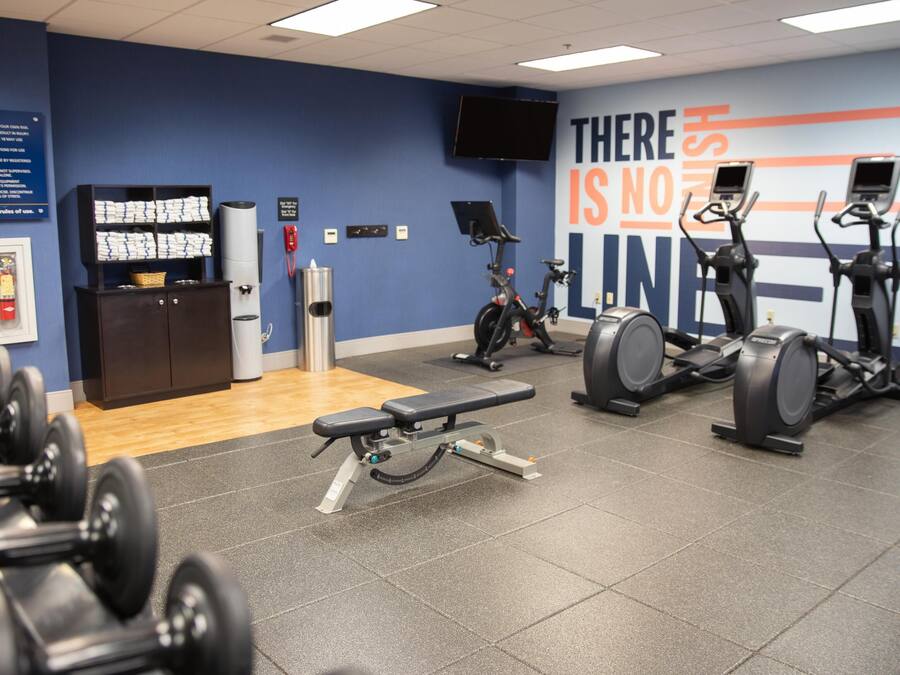 Un gimnasio con equipamiento de ejercicio, una banca y una pared con texto motivacional.