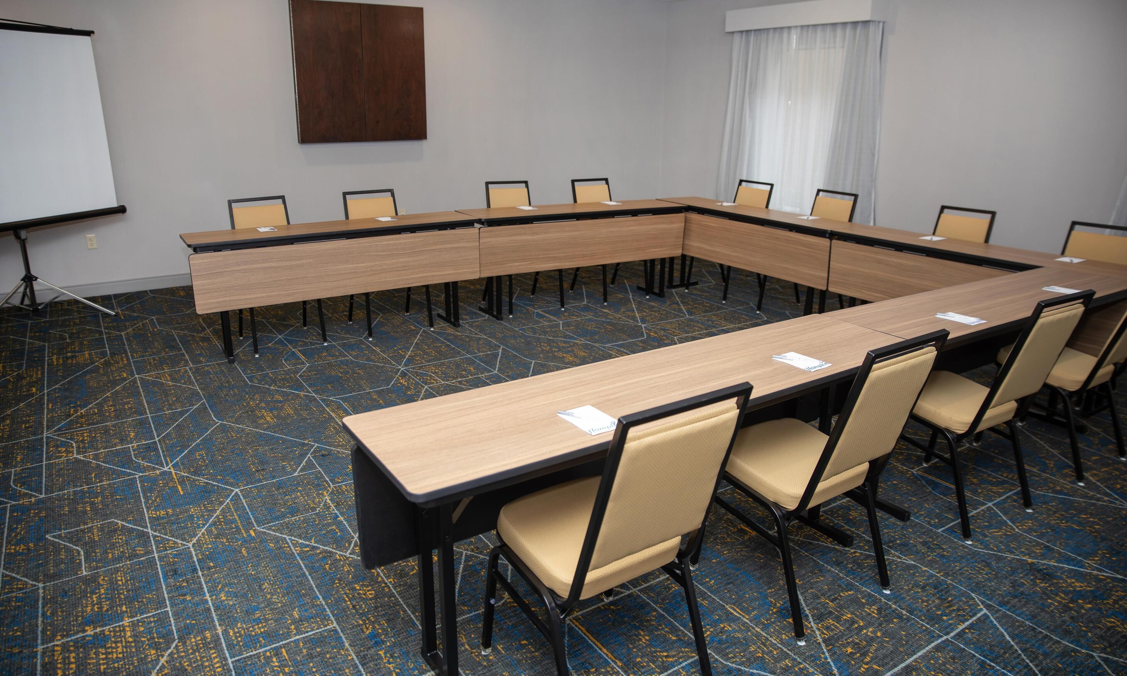 A conference room with a long table, chairs, a projector screen, and a whiteboard.