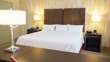 Habitación de hotel con una cama grande, dos mesitas de noche con lámparas, un escritorio con silla y un papel tapiz estampado.