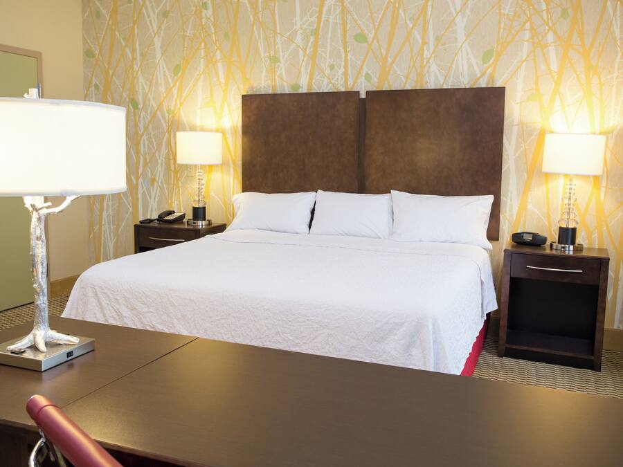 Habitación de hotel con una cama grande, dos mesitas de noche con lámparas, un escritorio con silla y un papel tapiz estampado.