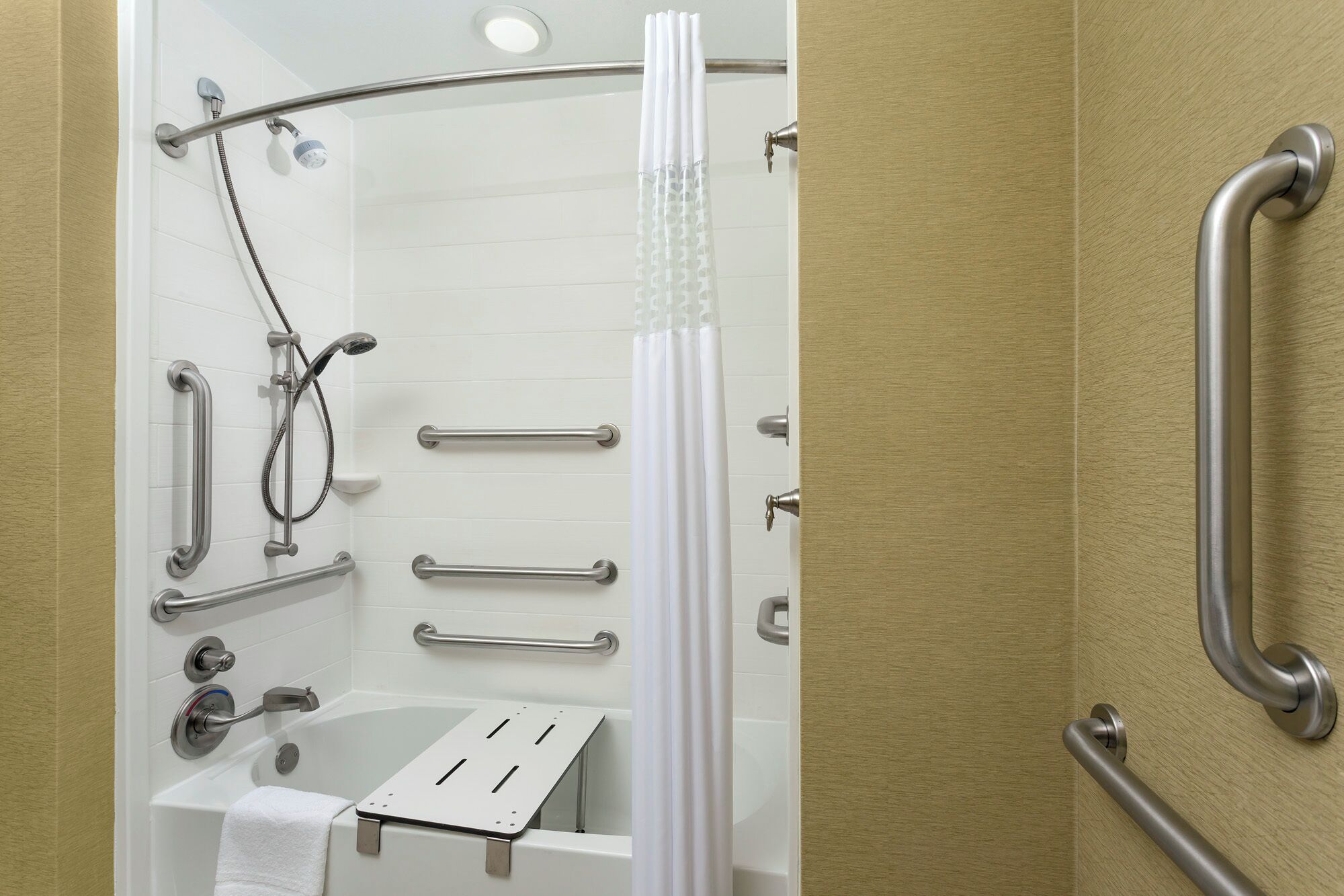 A bathroom with a bathtub, a shower with grab bars, and a toilet with a safety bar.