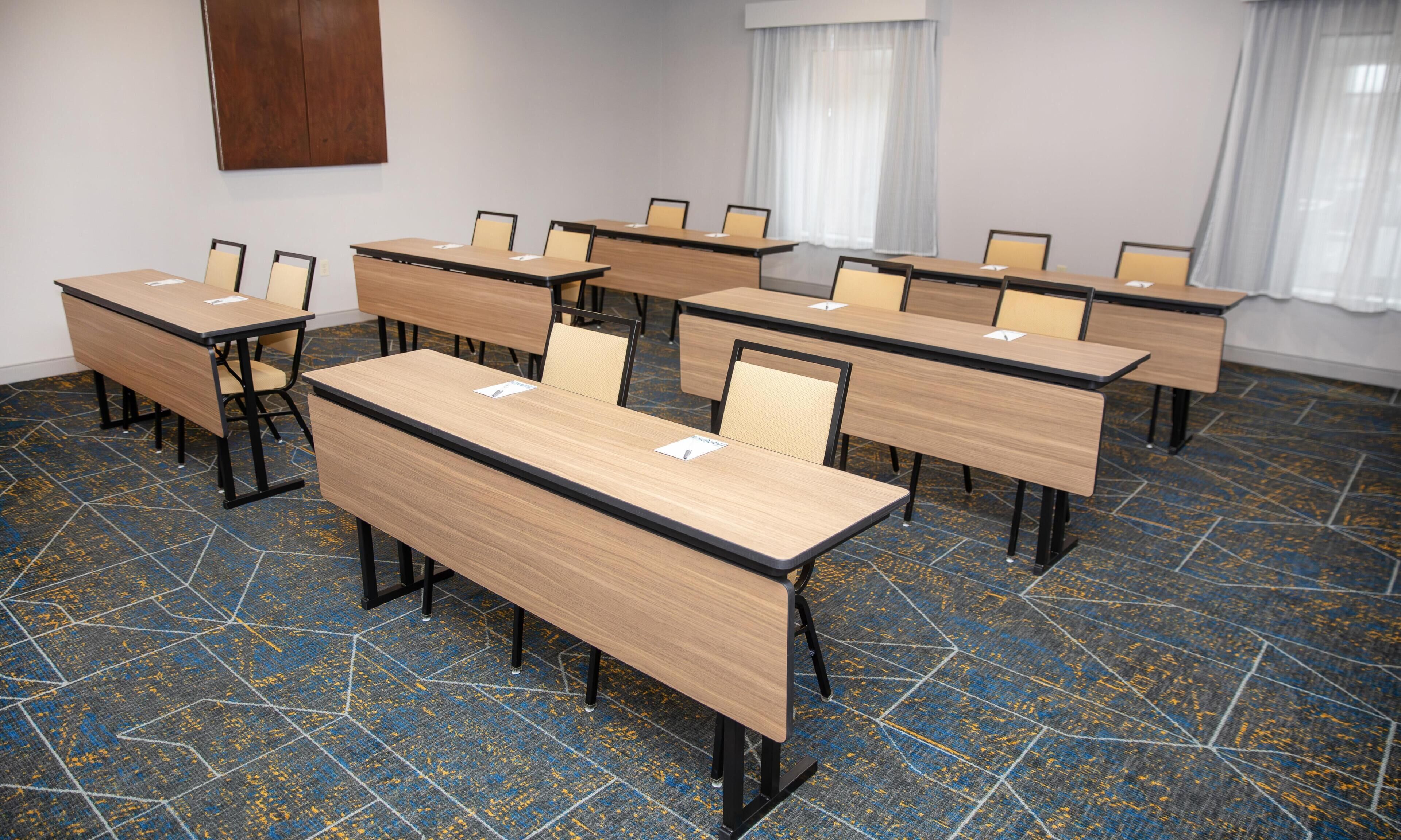A conference room with multiple tables and chairs, a patterned carpet, and a wooden accent wall.