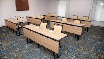 A conference room with multiple tables and chairs, a patterned carpet, and a wooden accent wall.