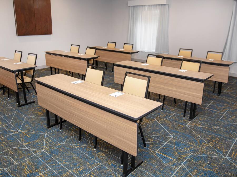 A conference room with multiple tables and chairs, a patterned carpet, and a wooden accent wall.