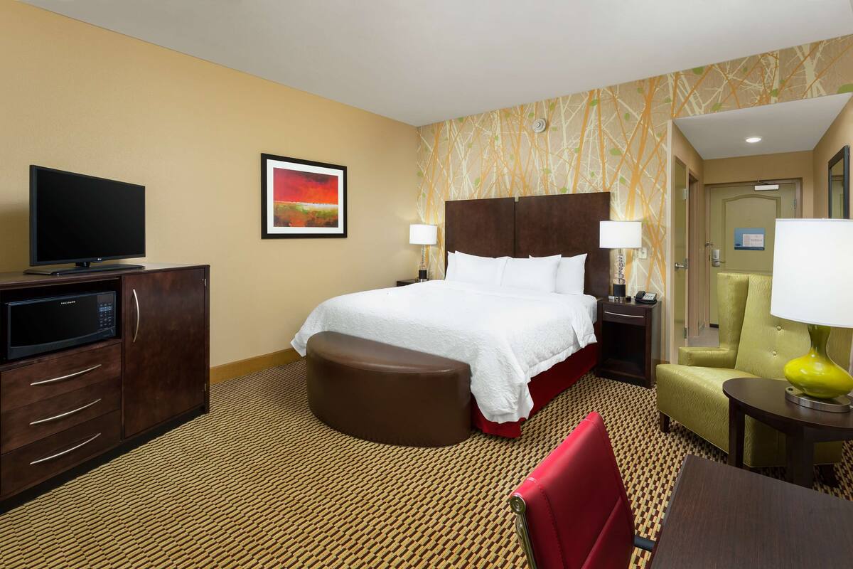 A hotel room with a bed, a television, a desk, a chair, and a lamp.