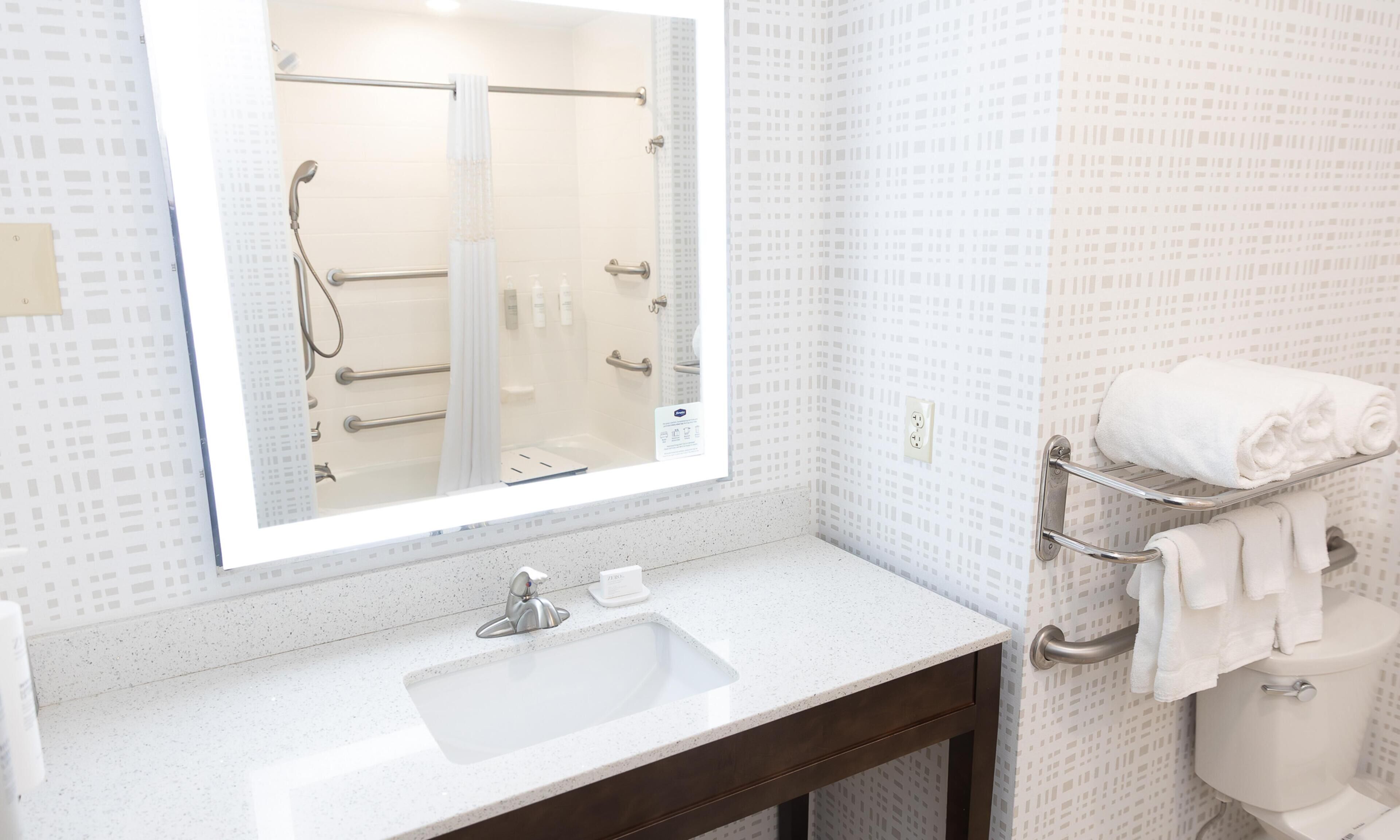 A bathroom with a large mirror, a sink, a shower, and a towel rack.