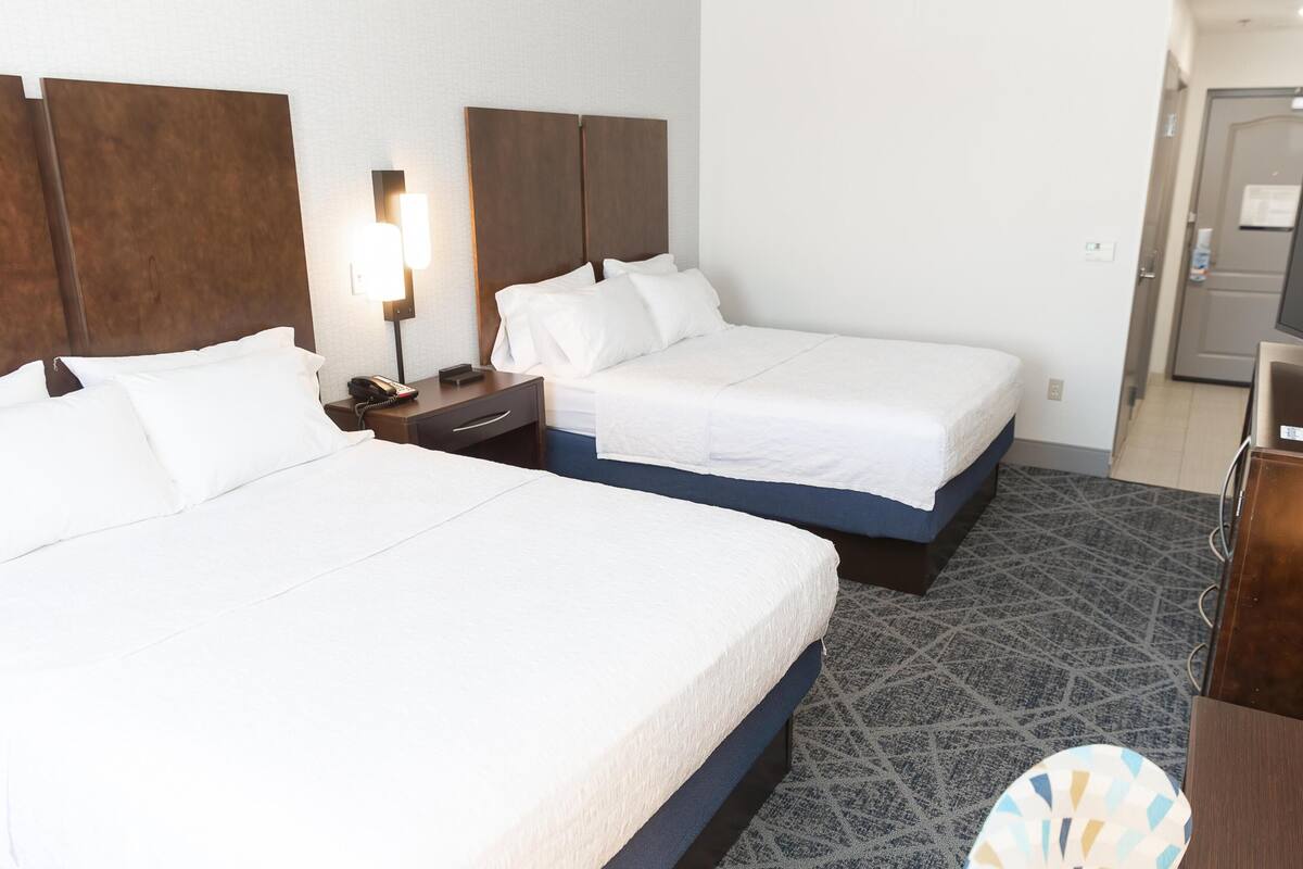 A hotel room with two beds, a desk, a lamp, a TV, and a patterned carpet.