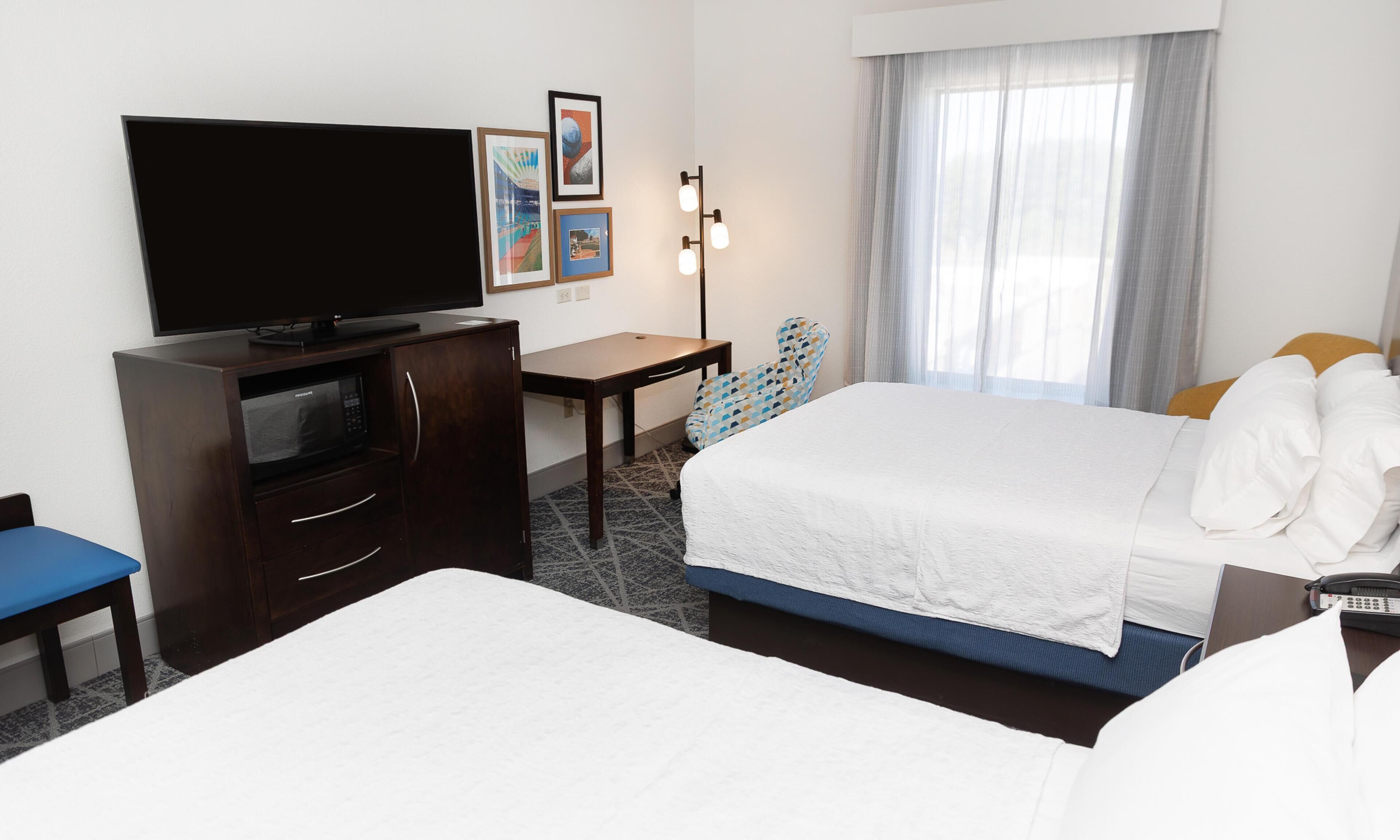A hotel room with a bed, a desk, a television, a chair, and a window with curtains.