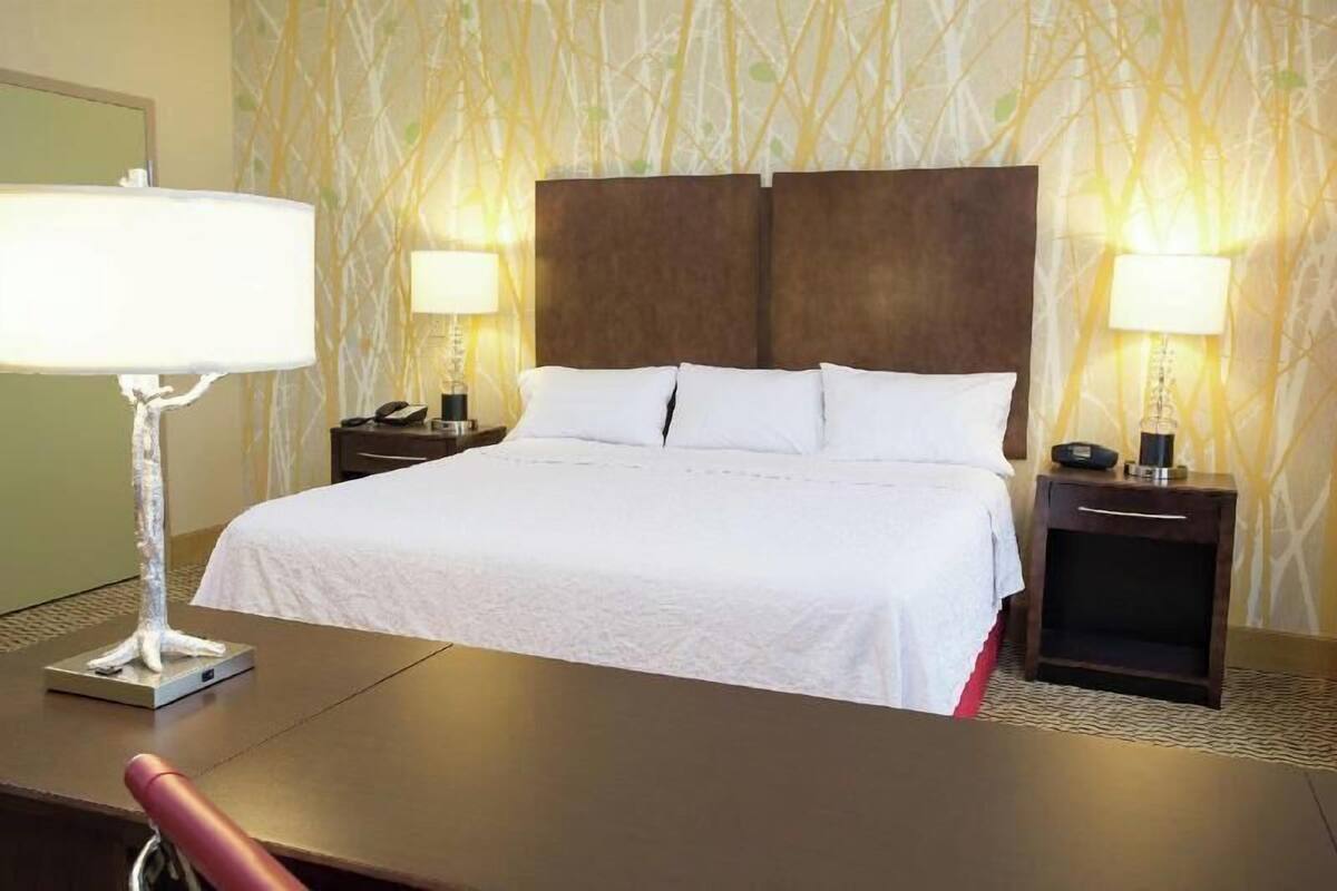 A hotel room with a large bed, two bedside tables with lamps, a desk, and a chair.