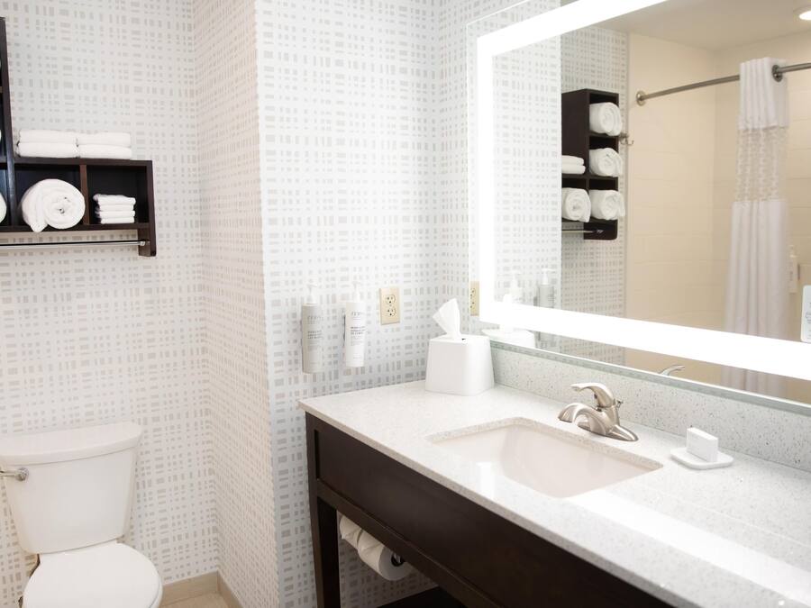 Une salle de bain avec des toilettes, un lavabo avec un miroir et des étagères avec des serviettes.
