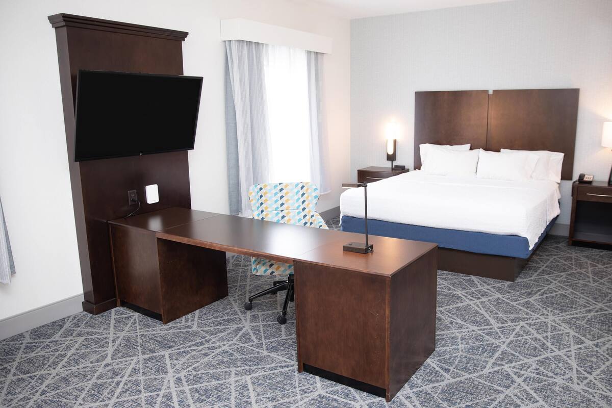 A hotel room with a large bed, a desk, a TV, and a nightstand with a lamp.