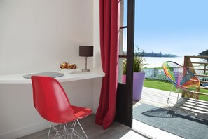 Une chambre moderne avec une chaise rouge, un ordinateur portable et un bol de fruits sur une étagère blanche.